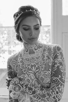 a woman wearing a white lace dress with a tiara on her head and arms crossed