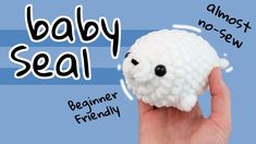 a hand holding a small white sheep toy with the words baby seal written on it