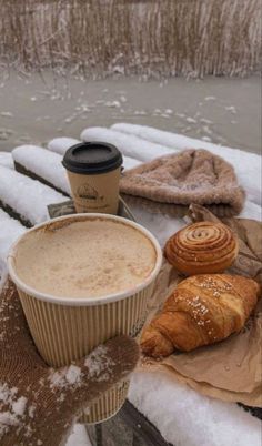 coffee and croissants are sitting on a bench in the snow next to some bread