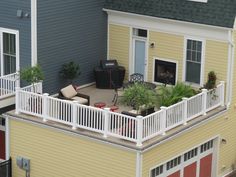 a balcony with furniture and plants on the top floor next to two story houses that are painted yellow and blue