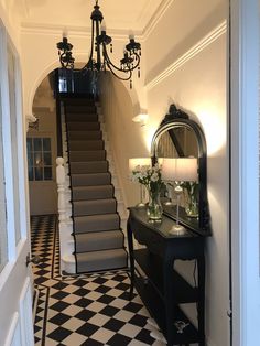 a hallway with black and white checkered flooring, chandelier and mirror