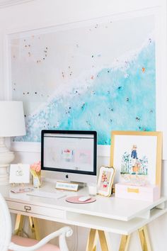 a white desk topped with a computer monitor next to a wall covered in pictures and paintings