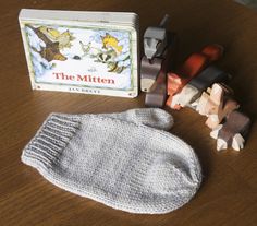 a knitted mitt next to a book and toy cars on a wooden table