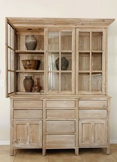 an old wooden cabinet with glass doors and vases on it's sideboard