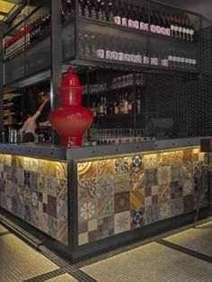 a red vase sitting on top of a counter next to a wall filled with bottles