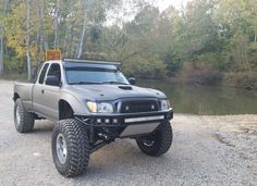 a gray truck parked on top of a gravel road next to a body of water