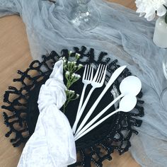 there are forks, spoons and knives on the black plate with white flowers in it