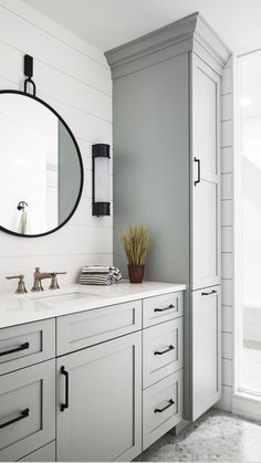 a white bathroom with gray cabinets and a round mirror