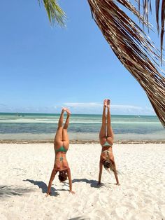 two women doing handstands on the beach with palm trees in the foreground