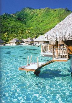 the water is crystal blue and there are some huts on stilts in the water