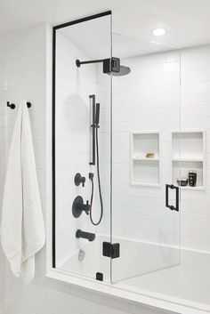 a white bathroom with black fixtures and glass shower door, towels hanging on the wall