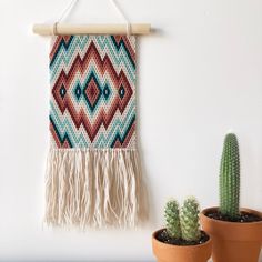 a wall hanging on the side of a white wall next to two potted cacti