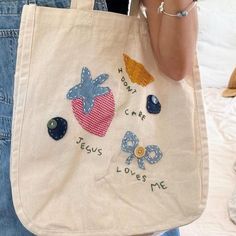 a woman is holding a bag with embroidered designs on it and the words jesus loves me