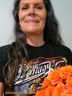 a woman with long hair holding a bunch of orange roses in her hands and smiling