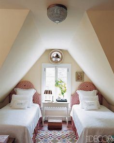 two twin beds in a room with white walls and carpeted flooring, one has a mirror on the wall