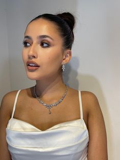 a woman in a white dress wearing a diamond necklace and earring with her hand on her hip