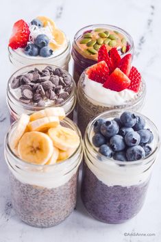 four jars filled with different types of food on top of a white counter next to blueberries, bananas and strawberries