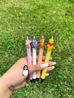 a person holding six different colored pencils in their hand on the grass with winnie the pooh stickers