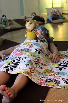 a young child laying on the floor under a blanket with stuffed animals in the background