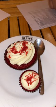 two cupcakes with white frosting and red sprinkles on a plate