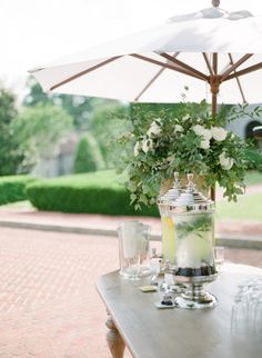 a table with an umbrella and some glasses on it, next to a potted plant