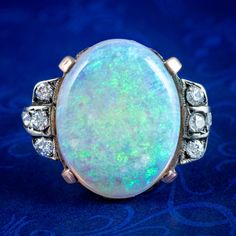 A striking antique Victorian opal statement ring boasting a magnificent natural opal cabochon weighing approx. 8 carats. It exhibits a changing kaleidoscope of greens, blues and purples with a warm orange glow behind. It's flanked by blocked shoulder accents dotted with six twinkling diamonds and further diamonds chasing into the band (approx. 0.30ct total).  Opal is the birthstone of October. Their magic has been revered throughout history, desired for their enchanting rainbow of colours that f Classic Cabochon Opal Ring, Antique Opal Ring With Oval Cabochon, Antique Oval Cabochon Opal Ring, Antique Opal Ring With Oval Cabochon Gemstone, Antique Oval Multi-stone Opal Ring, Heirloom Opal Cabochon Ring, Heirloom Cabochon Opal Ring, Antique Style Opal Ring For Formal Occasions, Victorian Style Opal Ring For Formal Occasions