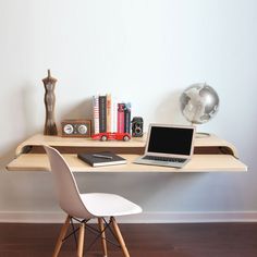 a laptop computer sitting on top of a wooden desk next to a white chair in front of a wall