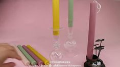 three different colored candles sitting next to each other on a pink surface with a hand reaching for them