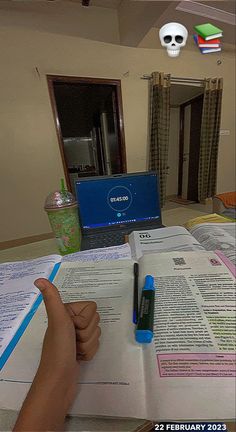 a hand pointing at an open book in front of a laptop computer on a desk