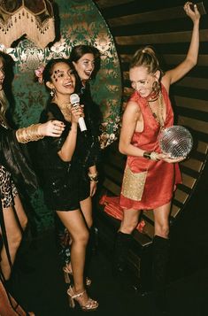 four women are standing in front of a wall holding microphones and singing into a mic