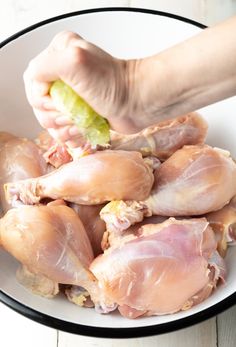 a person holding a piece of food in their hand over some raw chicken pieces on a white plate