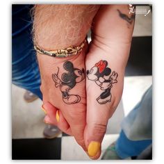 two people holding hands with mickey and minnie mouse tattoos on their fingers, one has a red bow in her hair