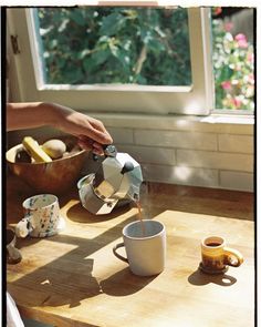 a person pours coffee into a cup on a wooden table in front of a window