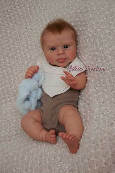 a baby is holding a stuffed animal on a bed with a white shirt and brown pants