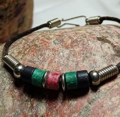 a close up of a bracelet on top of a rock with metal beads and leather cord