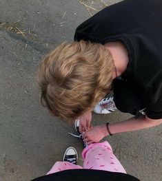 a young boy is tying his shoes on the ground while looking down at something in front of him