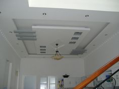 an empty room with white walls and ceiling fan in the center, stairs leading up to the second floor