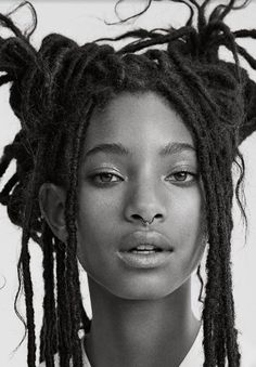 a black and white photo of a woman with dreadlocks on her head looking at the camera