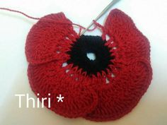 a crocheted red object with a black hole in the middle and thread on top