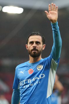 a man with a beard waves to the crowd while wearing a blue shirt and holding his hand in the air