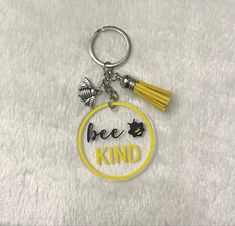 a keychain with the words bee kind on it, and a yellow tassel