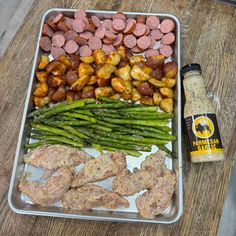 an assortment of meats, asparagus and sausages in a metal tray