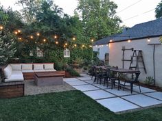 an outdoor patio with seating and lights strung over the back yard, surrounded by greenery