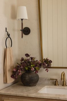 a bathroom sink with a mirror above it and flowers in a vase on the counter