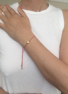 a woman wearing a red bracelet with a gold heart charm on it's wrist