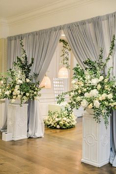 flowers are in white vases with drapes on the windowsill and curtains behind them