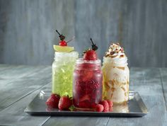 three mason jars filled with different types of drinks and topped with whipped cream, strawberries, and lemonade