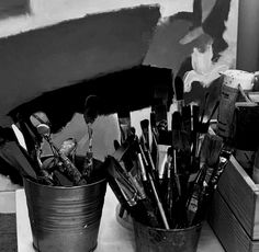 black and white photograph of paintbrushes in buckets on counter next to wall