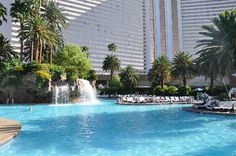 an outdoor pool surrounded by palm trees and water features a waterfall in the middle with lounge chairs around it