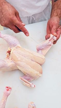 a man cutting up raw chicken on top of a white table with other meats